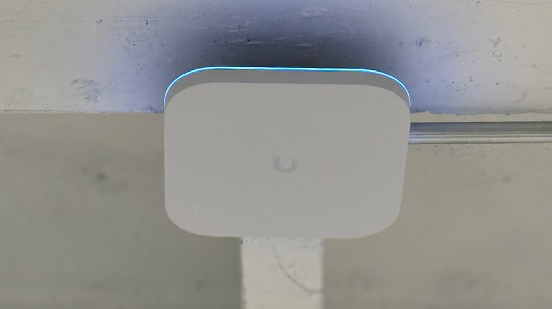 Ceiling mounted UniFi access point with glowing blue LED indicator and professional cable management conduit