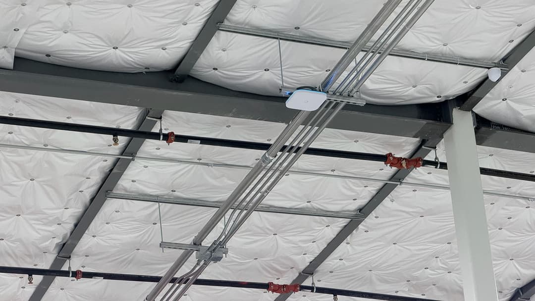 Commercial wireless access point installation on a warehouse ceiling with professional structured cabling