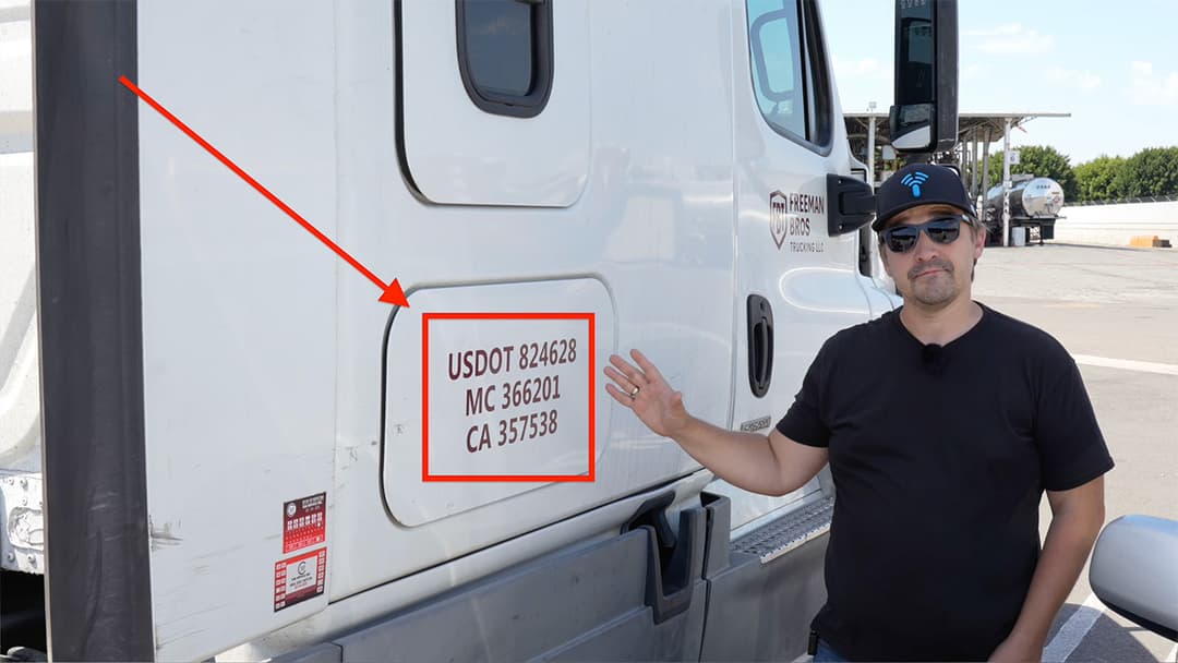 Engineer pointing to USDOT registration numbers and door panel identifiers on a commercial truck